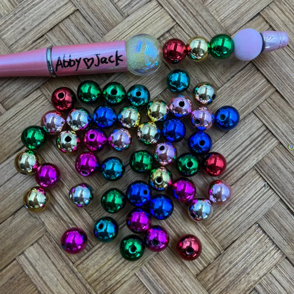 10MM metallic rainbow acrylic beads in assorted colors including blue, pink, green, red, and gold scattered on a woven surface next to a beadable pen labeled Abby and Jack.