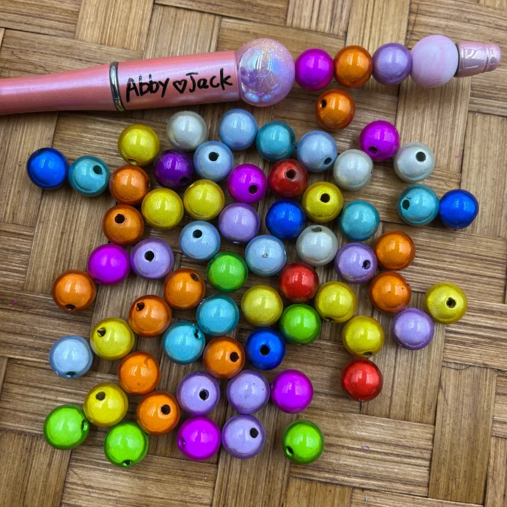 10MM rainbow miracle acrylic beads in assorted colors including pink, blue, orange, yellow, purple, green and teal with shimmery 3D illusion finish, shown next to a beadable pen on a wicker background.