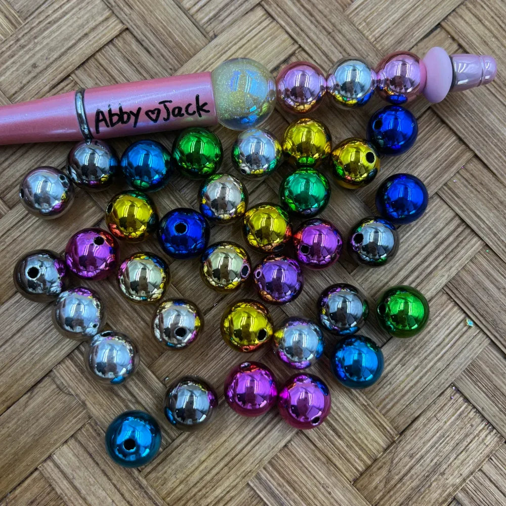 12MM metallic rainbow acrylic beads in assorted chrome colors including blue, green, gold, silver, pink, and purple displayed next to a beadable pen on a woven surface.