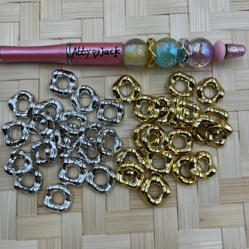 Gold and silver metallic wavy acrylic spacer beads displayed beside a pink beadable pen