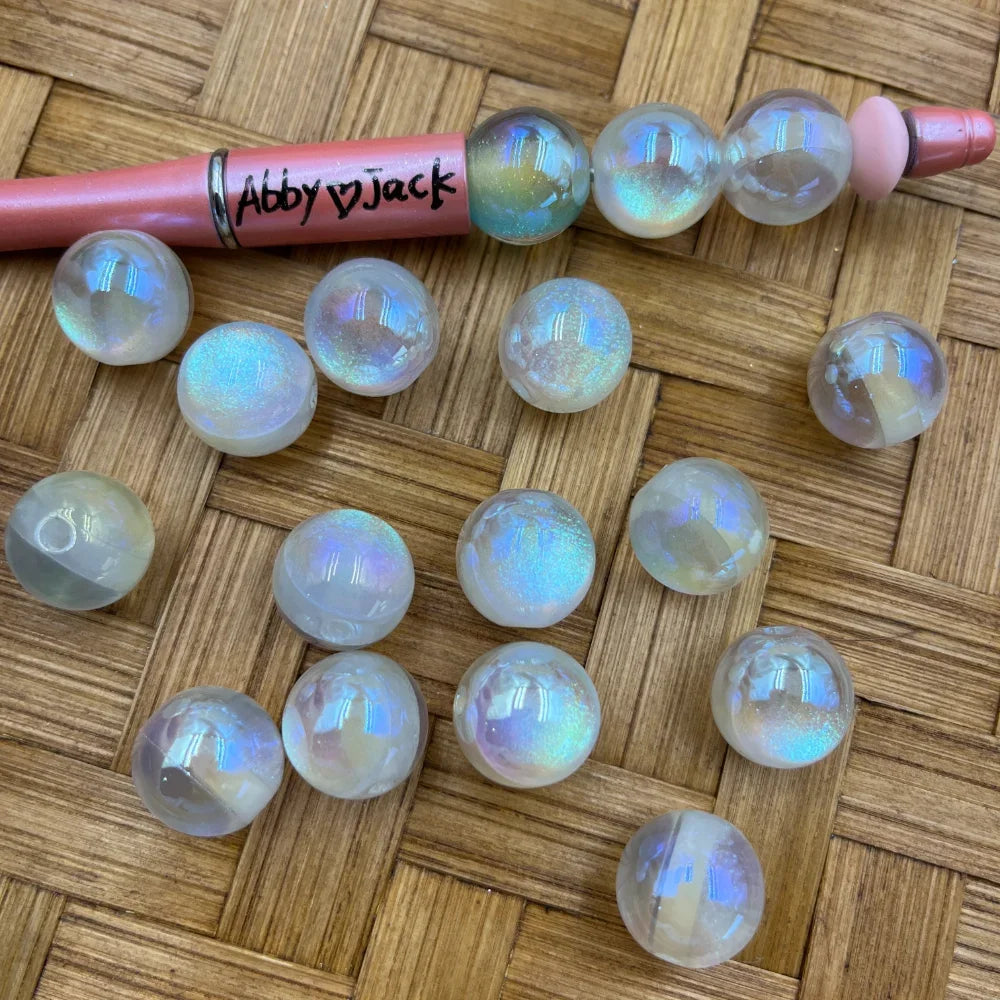 16MM aurora iridescent clear acrylic beads with rainbow holographic shimmer finish displayed on woven surface next to a beadable pen, perfect for DIY jewelry making and keychains.