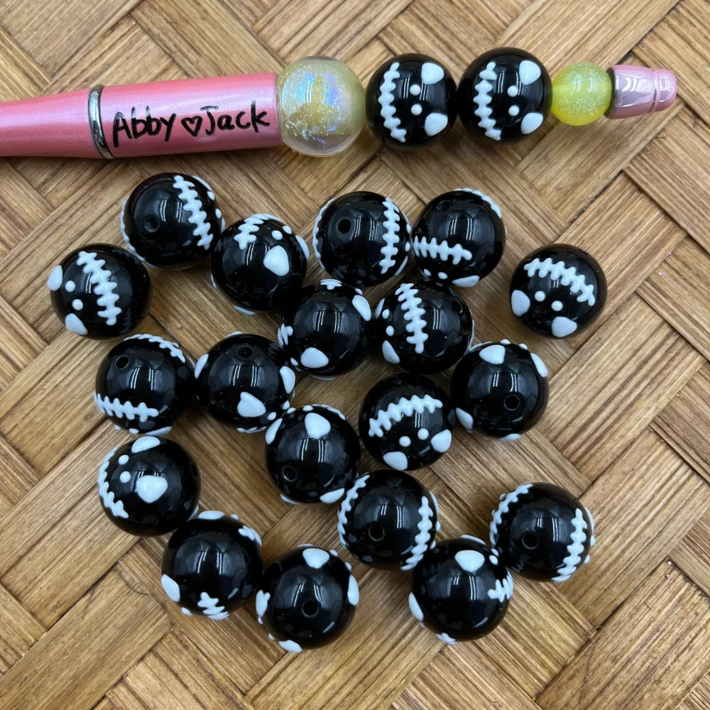 16MM black acrylic round beads with white Frankenstein stitch and bolt pattern, shown with a beadable pen on wicker surface