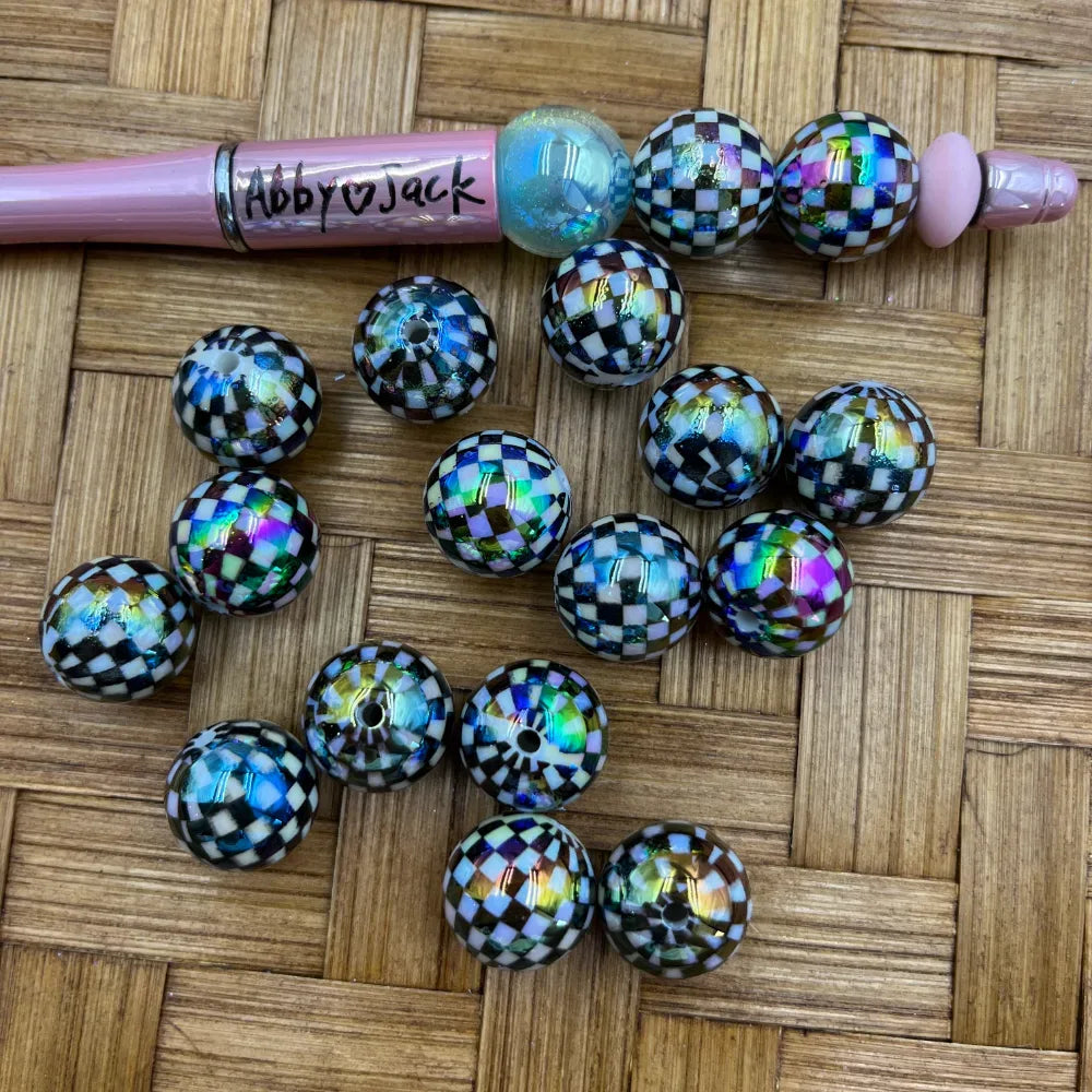 16MM black and white checkered iridescent acrylic beads with holographic shimmer finish, shown alongside a pink beadable pen on a wicker surface