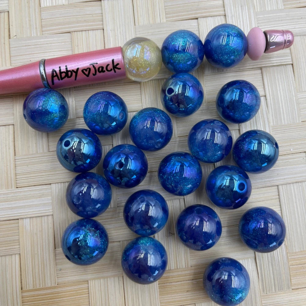16MM blue galaxy glitter acrylic beads with iridescent shimmer and confetti flakes, shown with a beadable pen on a wicker surface