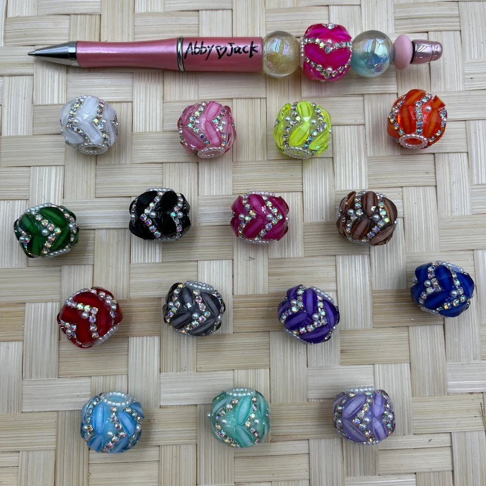 Assorted round bling swirl acrylic fancy beads with rhinestone and pearl accents displayed beside a pink beadable pen