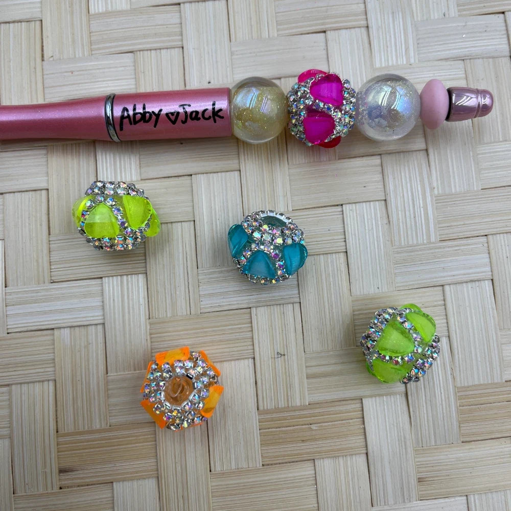Assorted neon acrylic cage fancy beads with AB rhinestones displayed beside a pink beadable pen