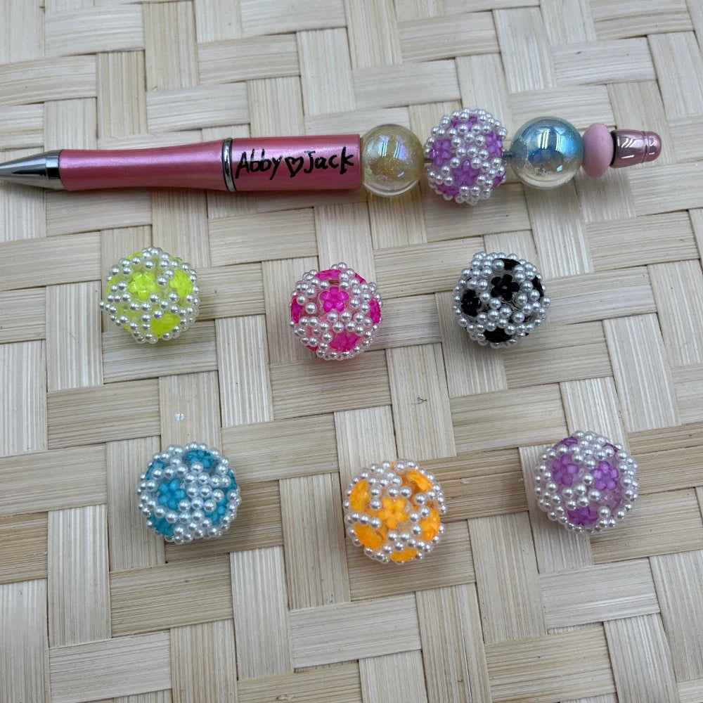 Assorted pearl flower acrylic fancy beads in yellow, pink, black, blue, orange, and purple shown beside a pink beadable pen.