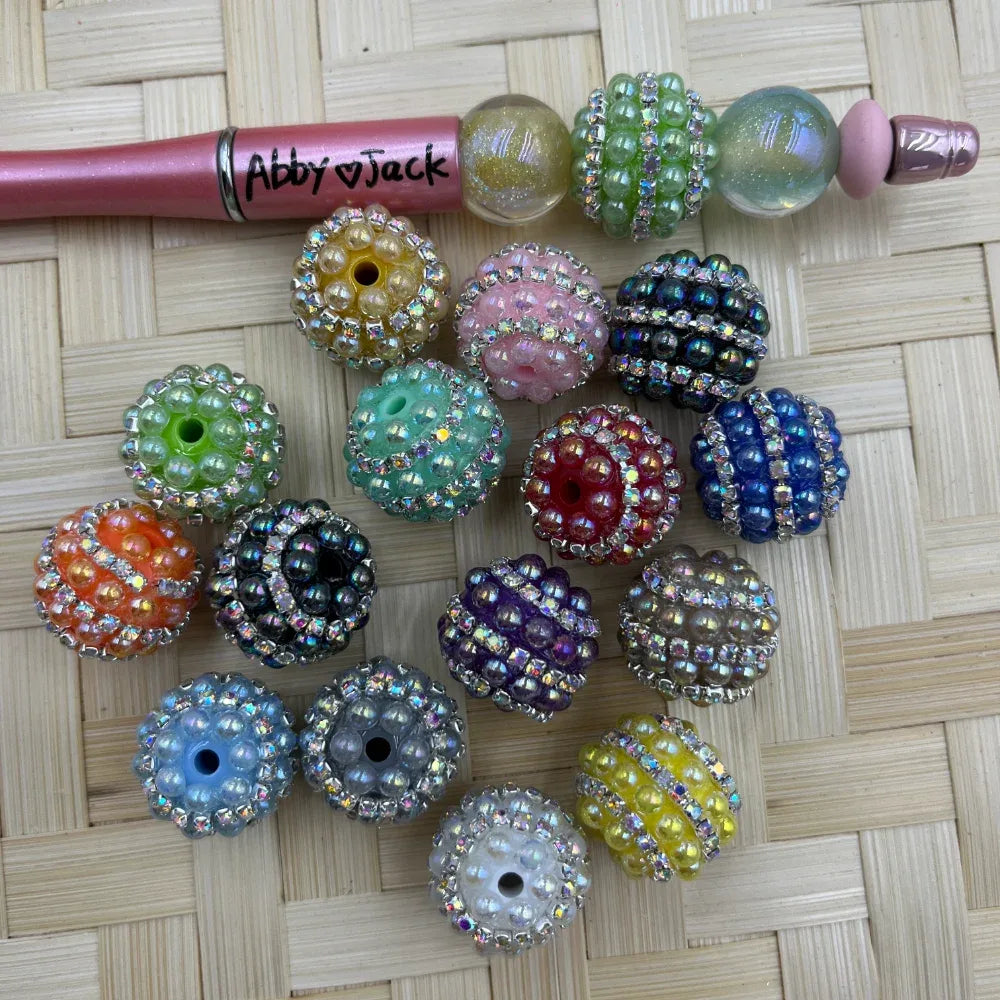 Assorted round pearl rhinestone acrylic fancy beads in pastel and bold colors beside a beadable pen