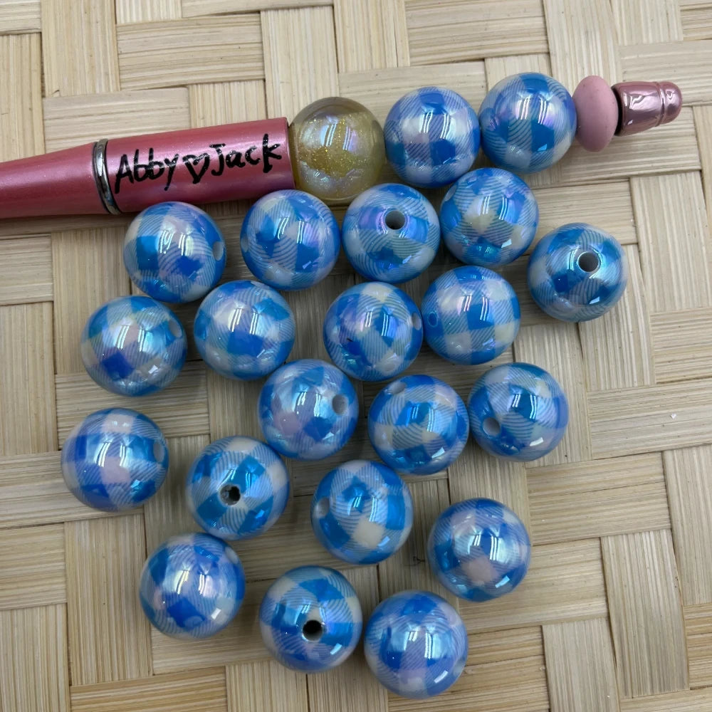 20MM blue buffalo plaid iridescent AB acrylic beads with shiny aurora borealis finish, shown next to a beadable pen on wicker background.