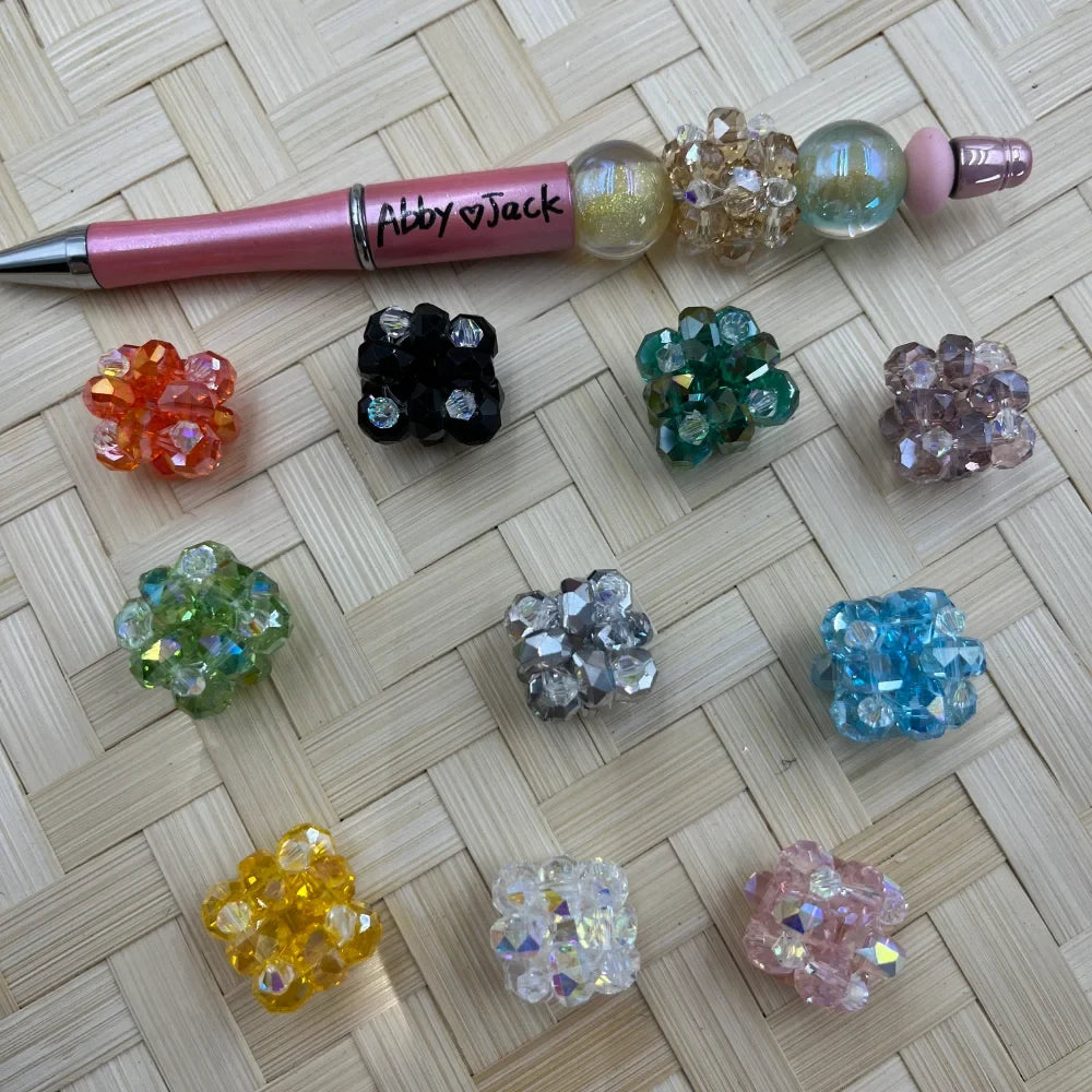 20MM crystal cluster ball fancy beads in 10 colors including orange, black, teal, mauve, green, silver, blue, yellow, clear, and pink displayed on woven surface with a beadable pen
