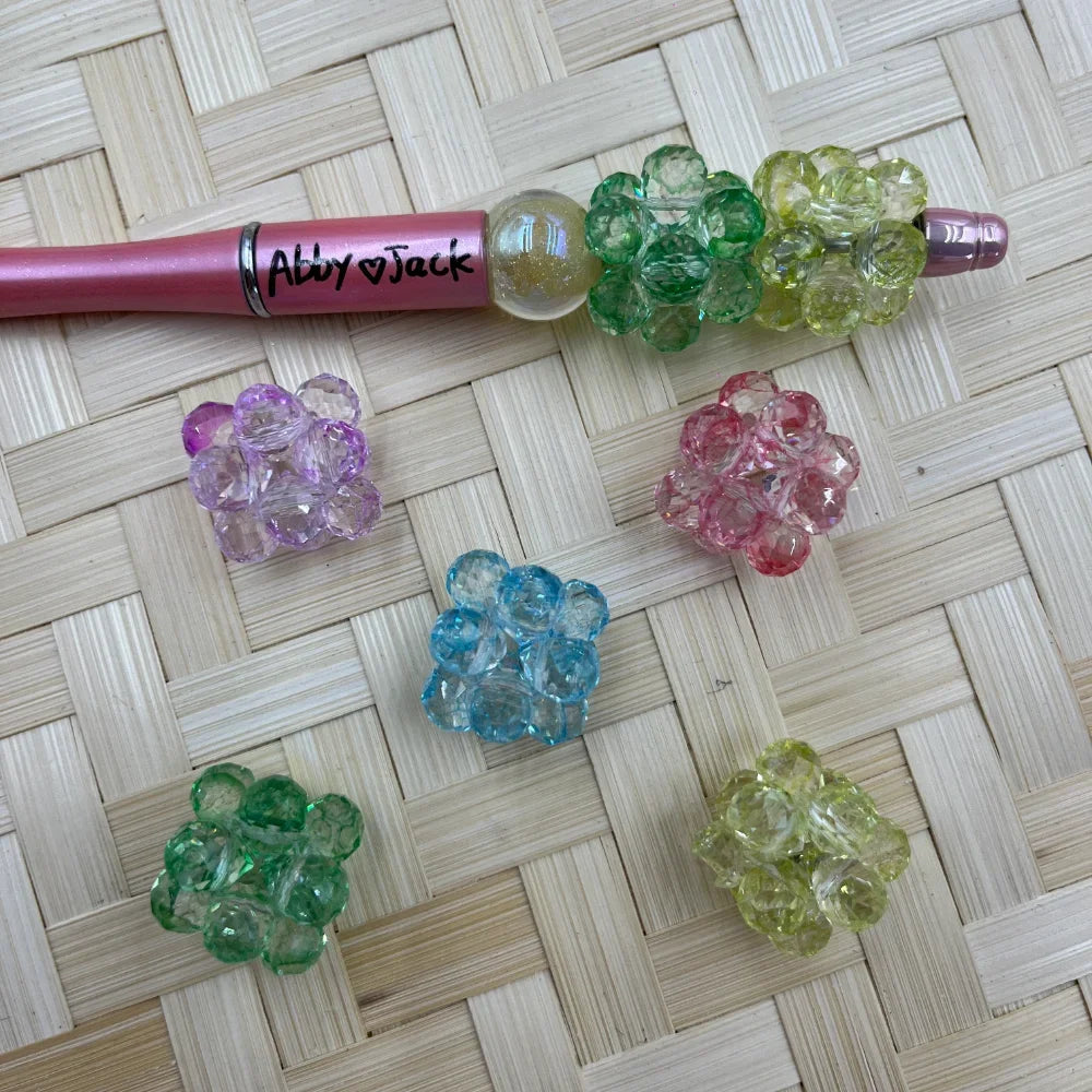 20MM faceted crystal cluster ball beads in pastel purple, pink, blue, green, and yellow-green colors displayed on woven surface with a pink beadable pen labeled Abby Jack