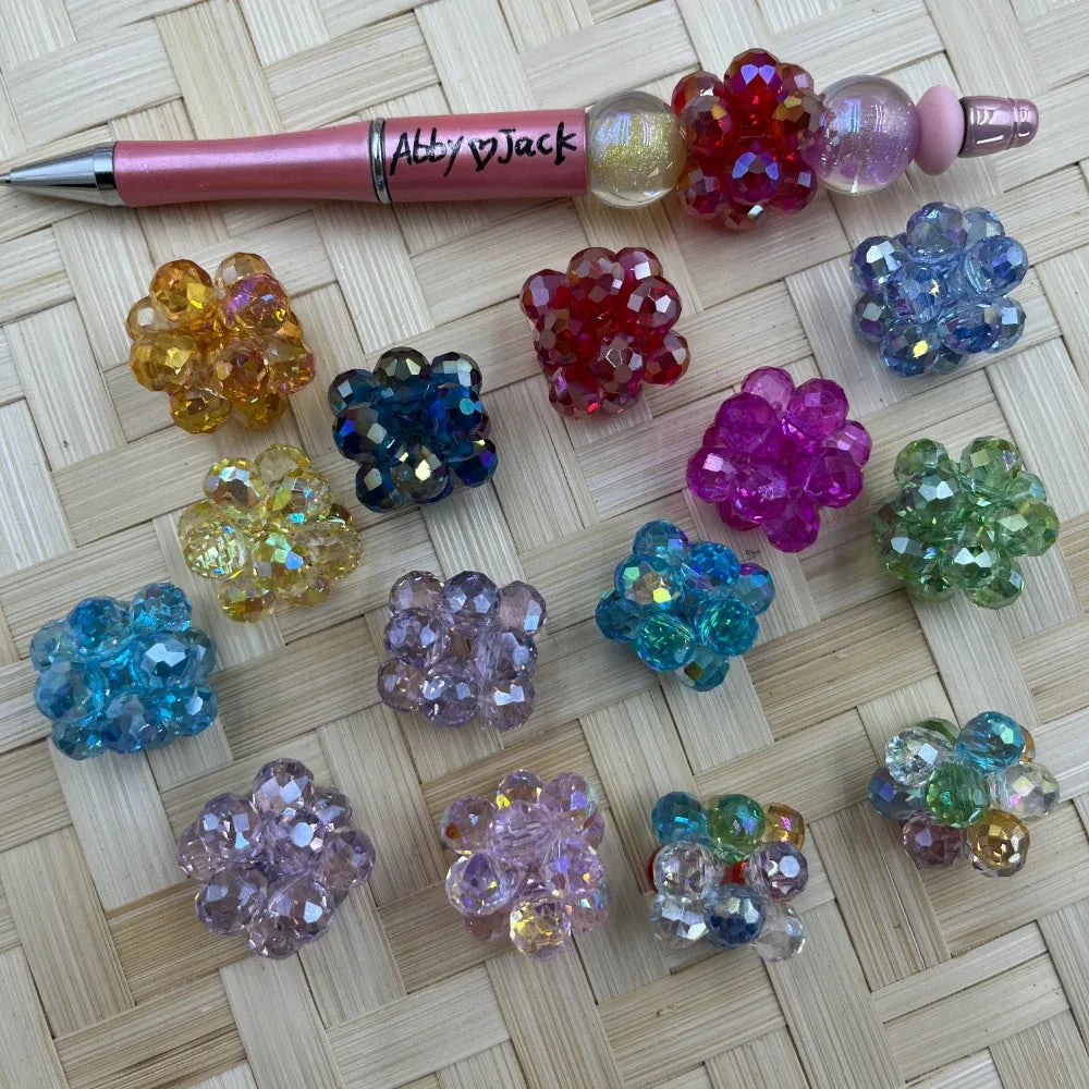 20MM faceted crystal flower cluster fancy beads in assorted colors including red, pink, blue, teal, purple, green, orange, and multicolor, displayed on woven surface next to a beadable pen.