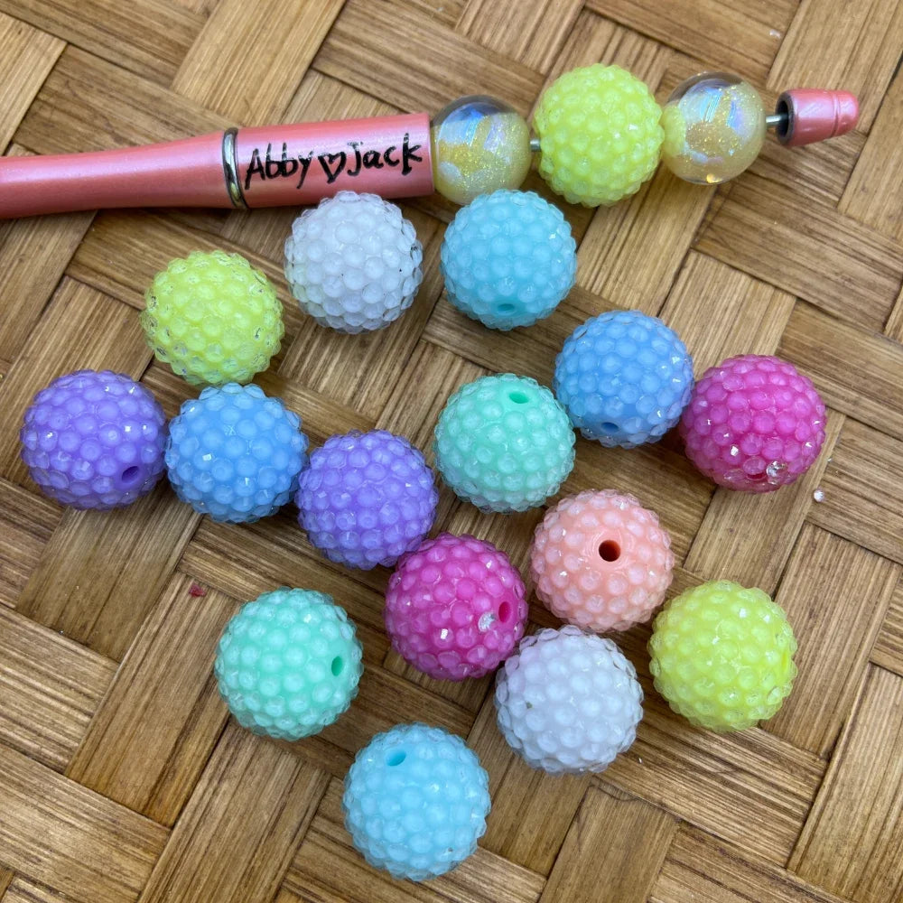 20MM pastel bumpy rhinestone acrylic beads in assorted colors including purple, blue, mint, pink, peach, yellow, and white, displayed on a woven surface next to a beadable pen.