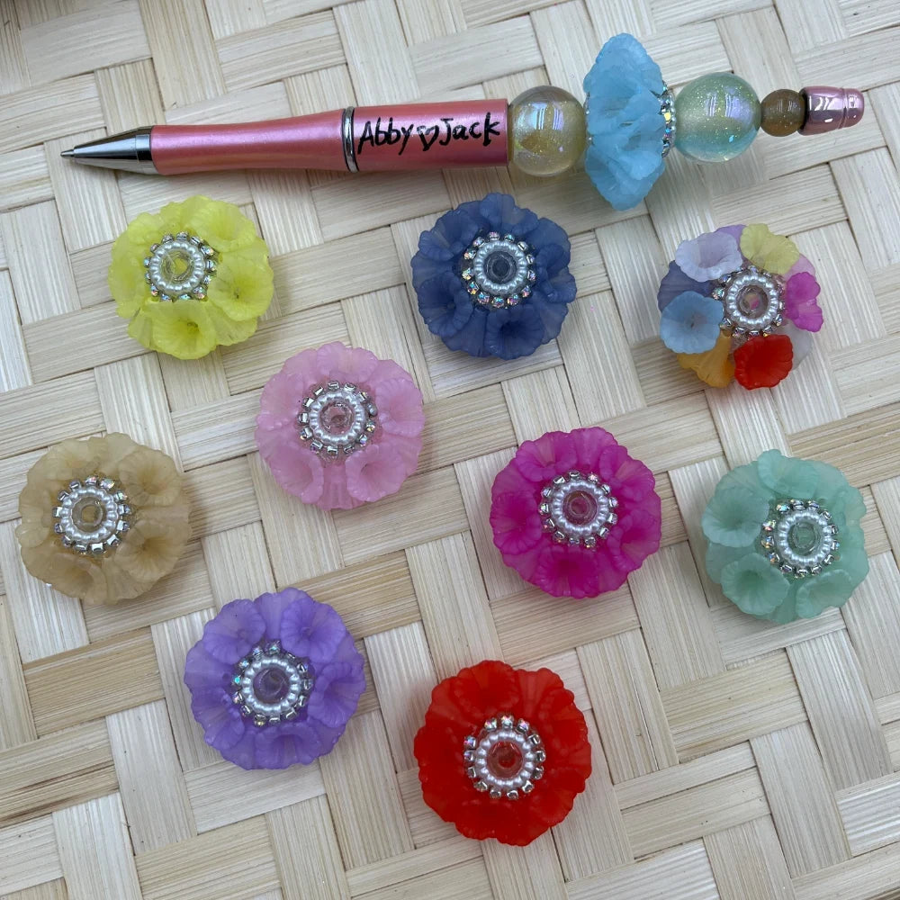 Assorted frosted flower acrylic fancy beads with rhinestone centers displayed beside a decorated beadable pen