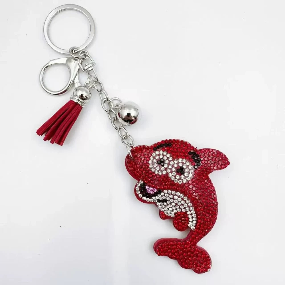 Four rhinestone dolphin charms in pink, aqua, black, and red with silver-tone rings, bells, and tassels on a white background. - Red