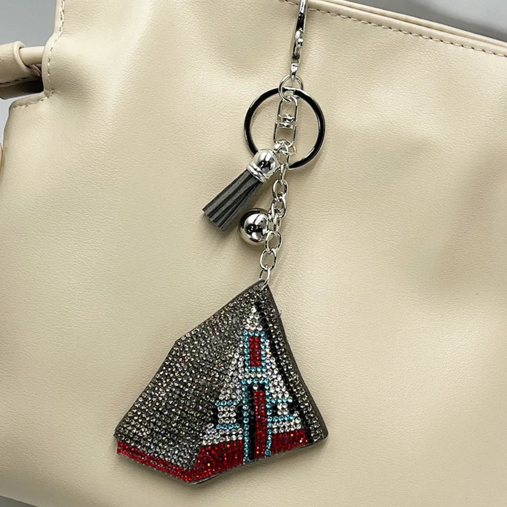 Crystal rhinestone teepee-shaped keychain charm with red, blue, and silver stones, tassel accent, attached to cream leather handbag
