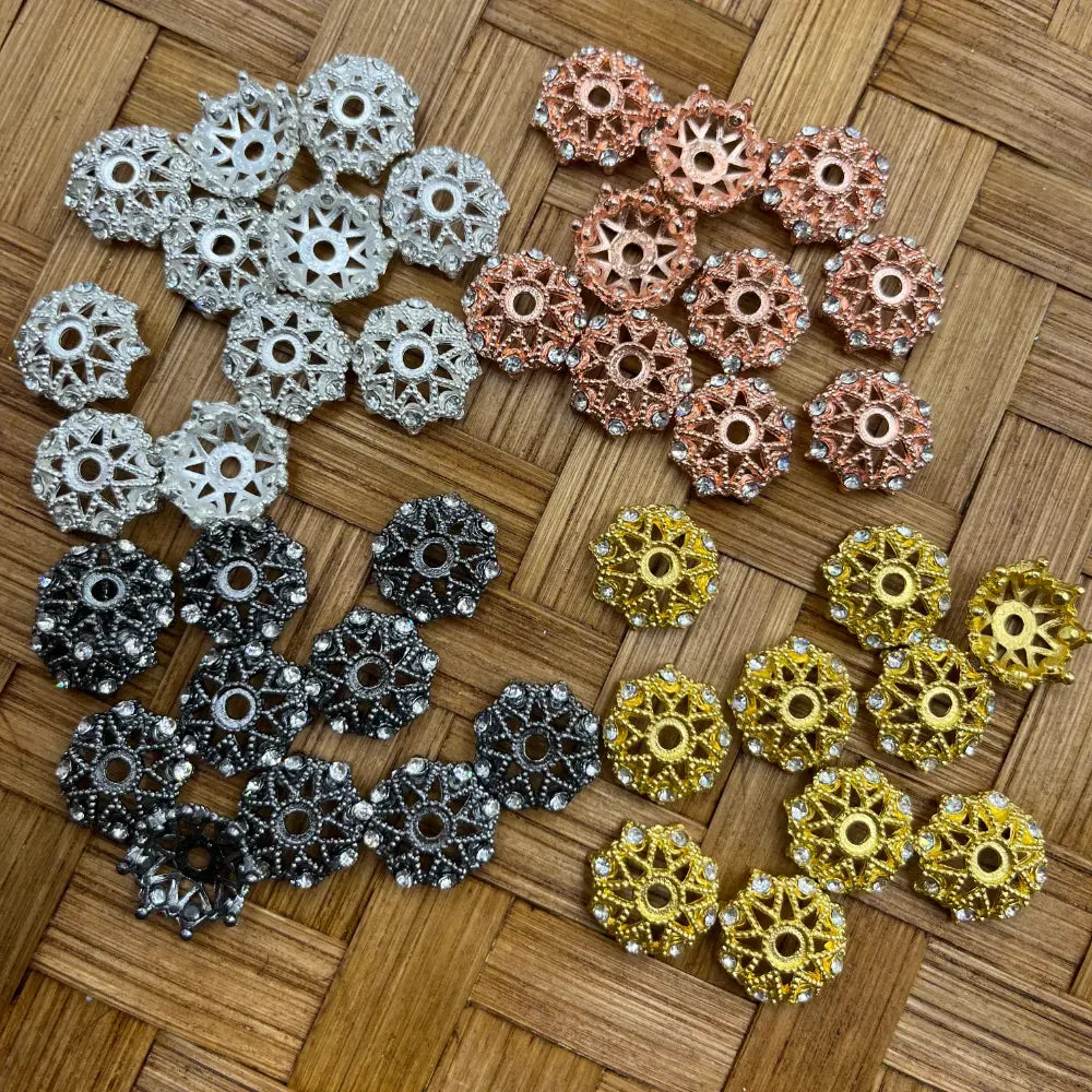 Assorted filigree rhinestone metal bead caps in silver, rose gold, gunmetal black, and gold, displayed on a woven bamboo surface for DIY jewelry making and beadable pens.