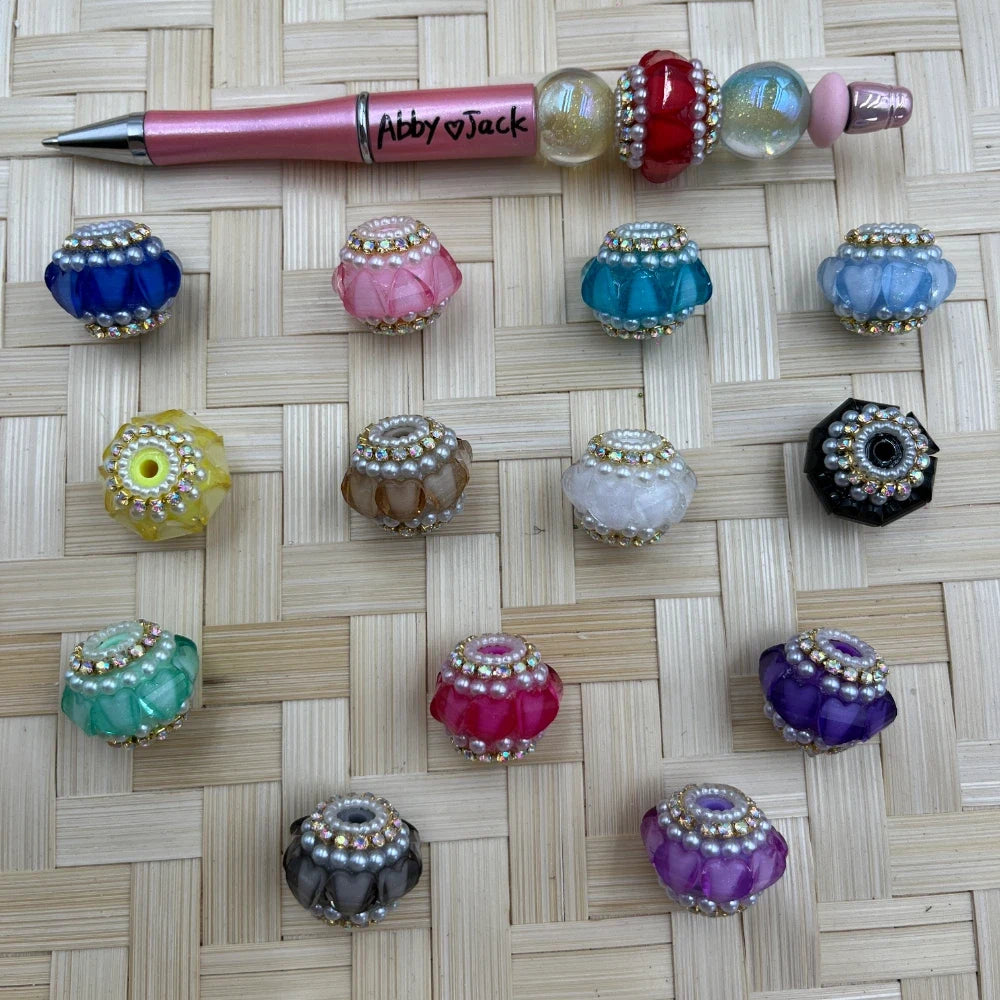 Assorted large hole faceted acrylic fancy beads with pearl and rhinestone trim displayed next to a pink beadable pen
