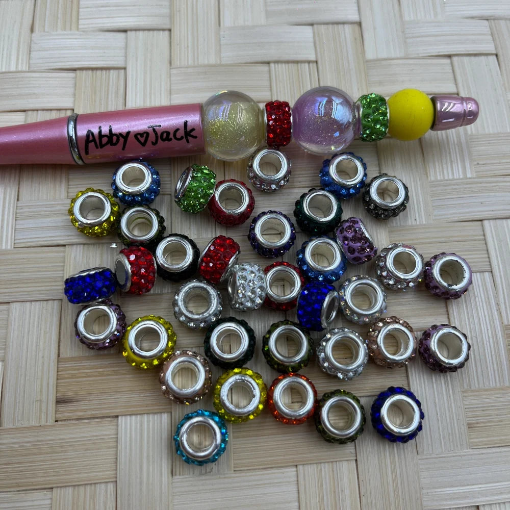 Assorted multicolor rhinestone large-hole metal spacer beads shown beside a pink beadable pen