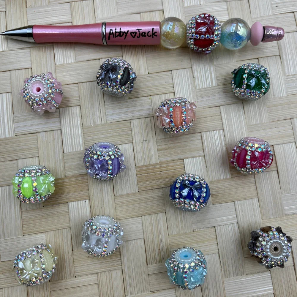 Assorted large floral resin fancy beads with AB rhinestone trim displayed next to a pink beadable pen