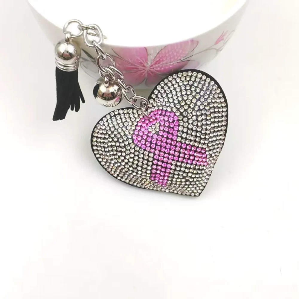 Two pink ribbon awareness rhinestone keychain charms on a white background, including a silver heart with pink ribbon and a pink awareness ribbon charm with tassels. - 1