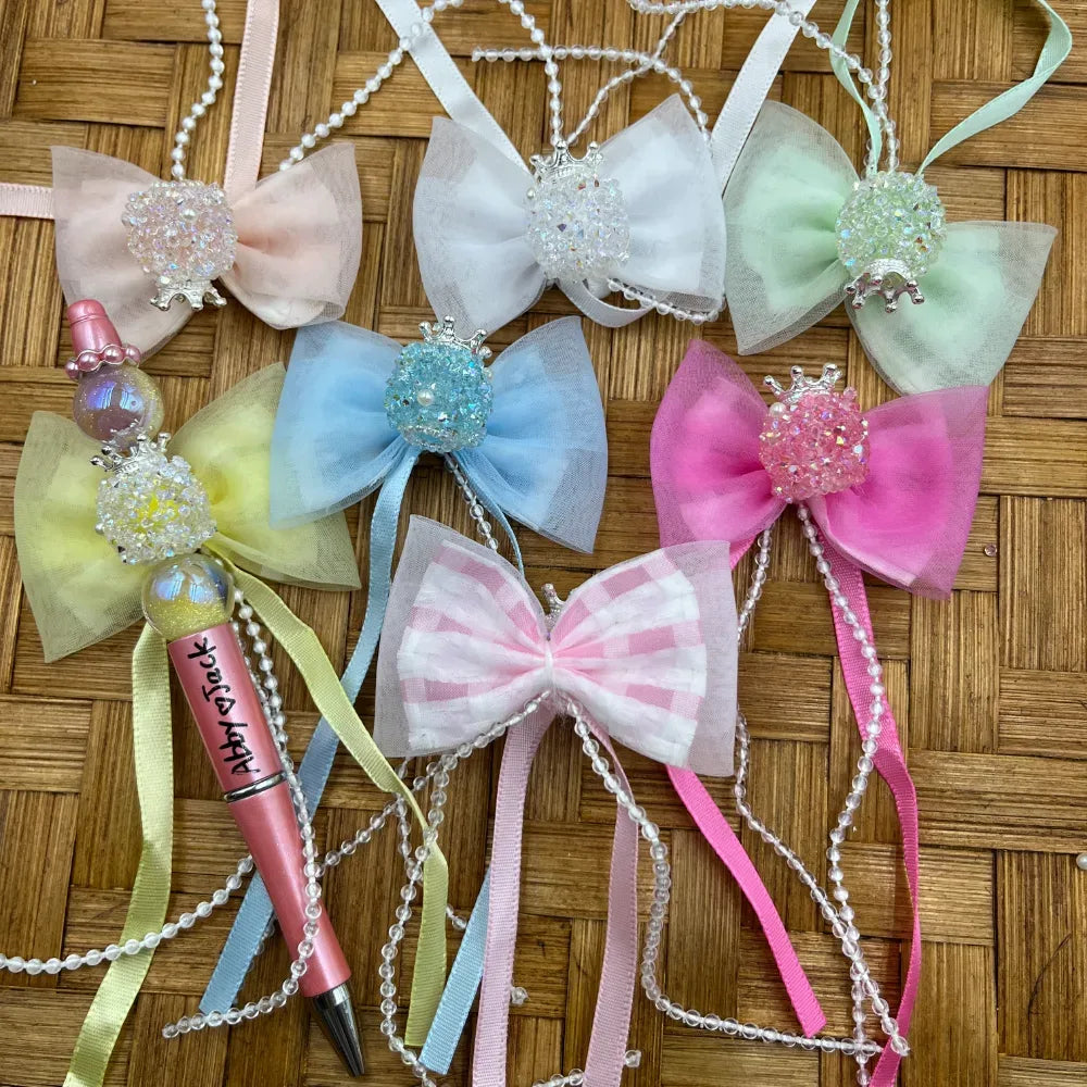 Pastel crystal rhinestone ball fancy beads in pink, white, blue, green, and yellow with tulle bows and pearl strands on woven bamboo background, used for beadable pens and DIY crafts