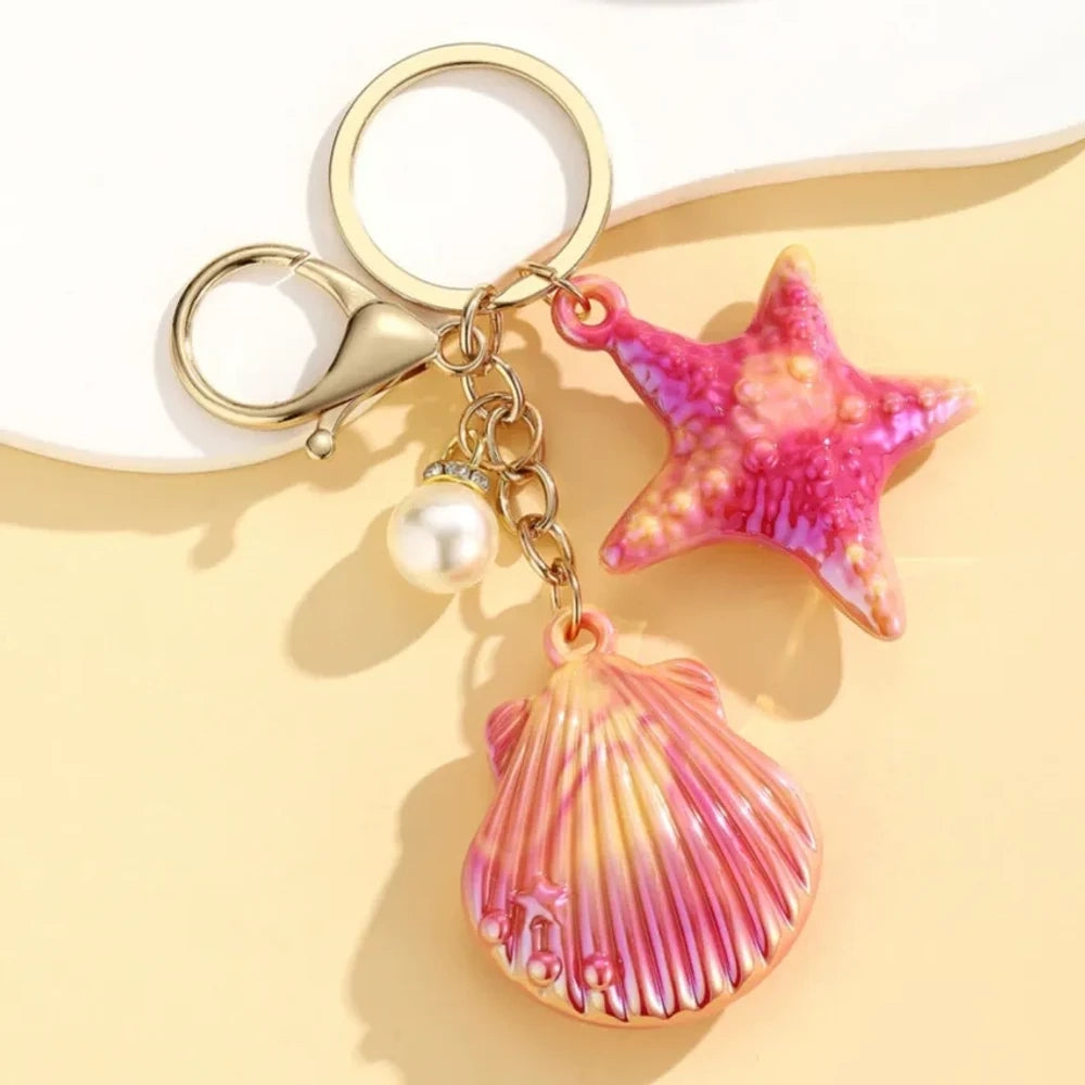 Six colorful resin ocean shell and starfish keychain charms with pearl beads in pink, white, purple, blue, iridescent, and hot pink, displayed on a yellow background. - 2
