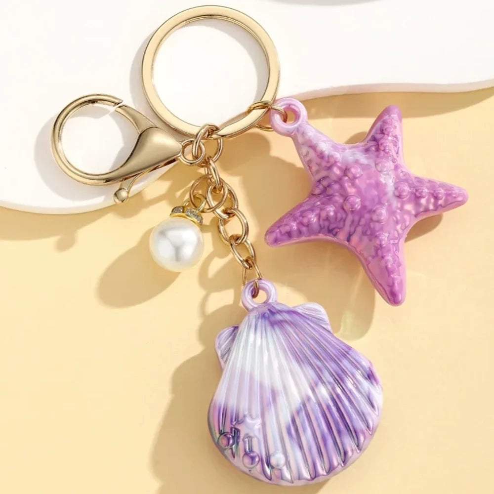 Six colorful resin ocean shell and starfish keychain charms with pearl beads in pink, white, purple, blue, iridescent, and hot pink, displayed on a yellow background. - 3