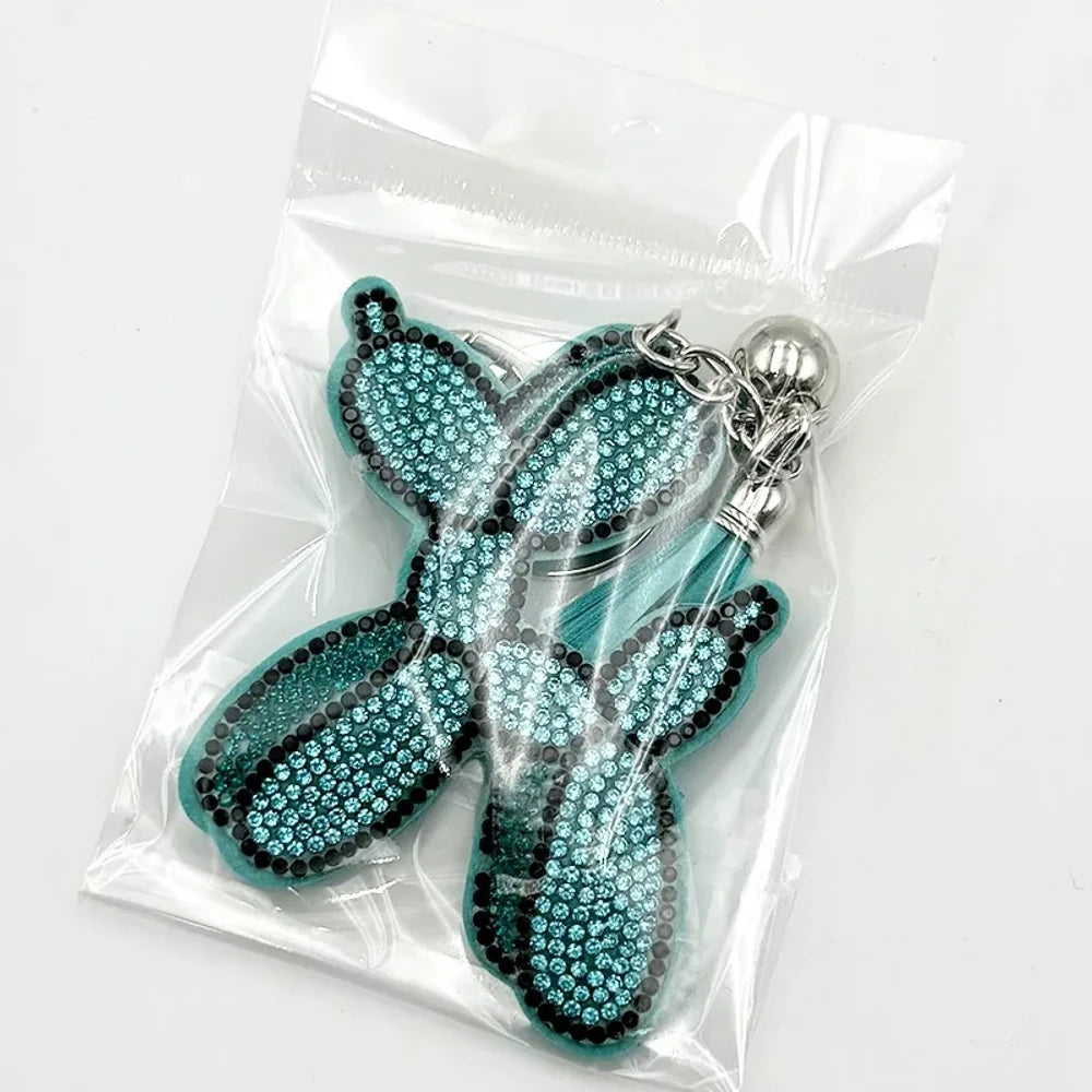 Five rhinestone-covered balloon dog keychain charms in green, yellow, brown, teal, and purple packaged in clear plastic bags on white background. - Blue