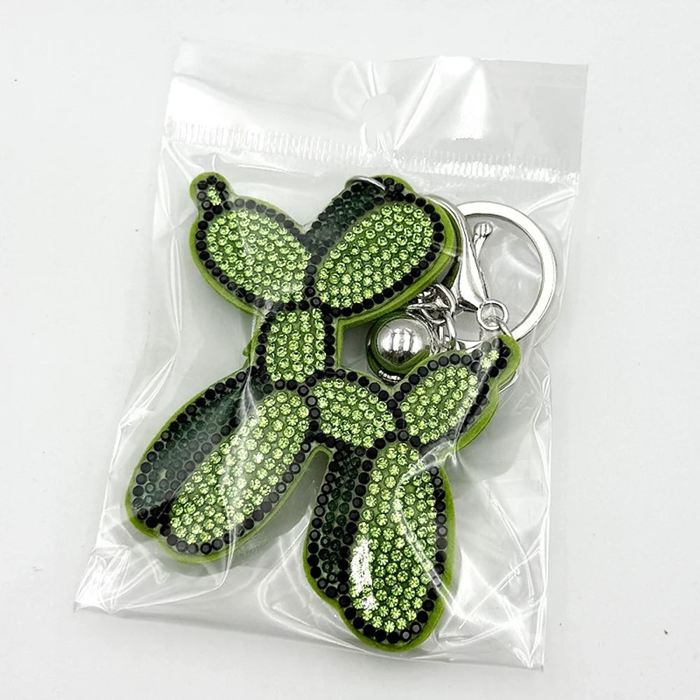 Five rhinestone-covered balloon dog keychain charms in green, yellow, brown, teal, and purple packaged in clear plastic bags on white background. - Green