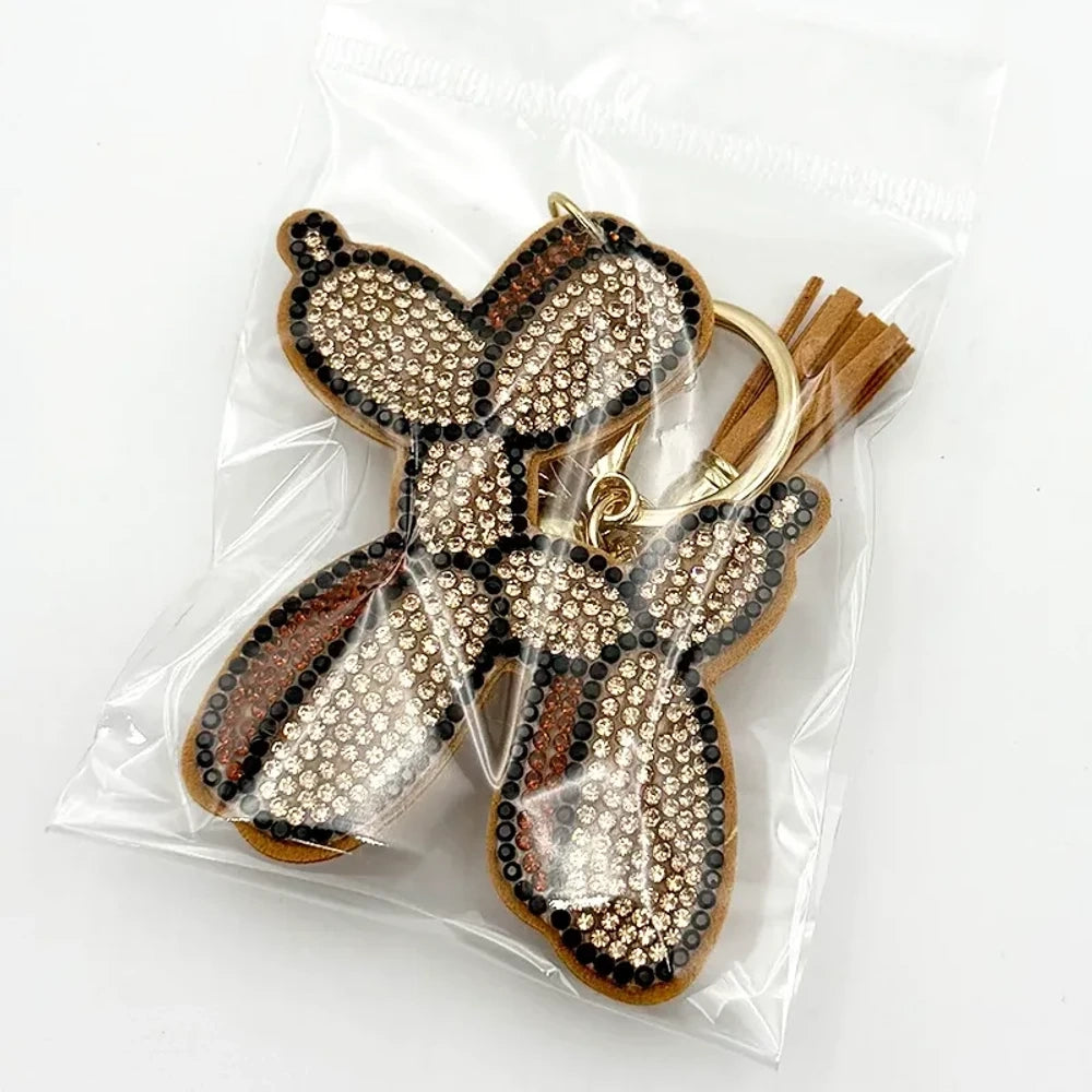 Five rhinestone-covered balloon dog keychain charms in green, yellow, brown, teal, and purple packaged in clear plastic bags on white background. - Khaki