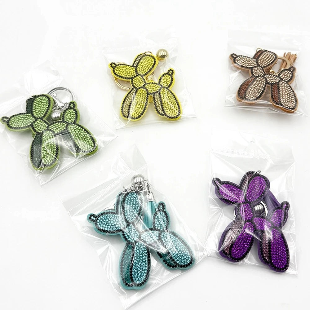 Five rhinestone-covered balloon dog keychain charms in green, yellow, brown, teal, and purple packaged in clear plastic bags on white background. - Random Mixed