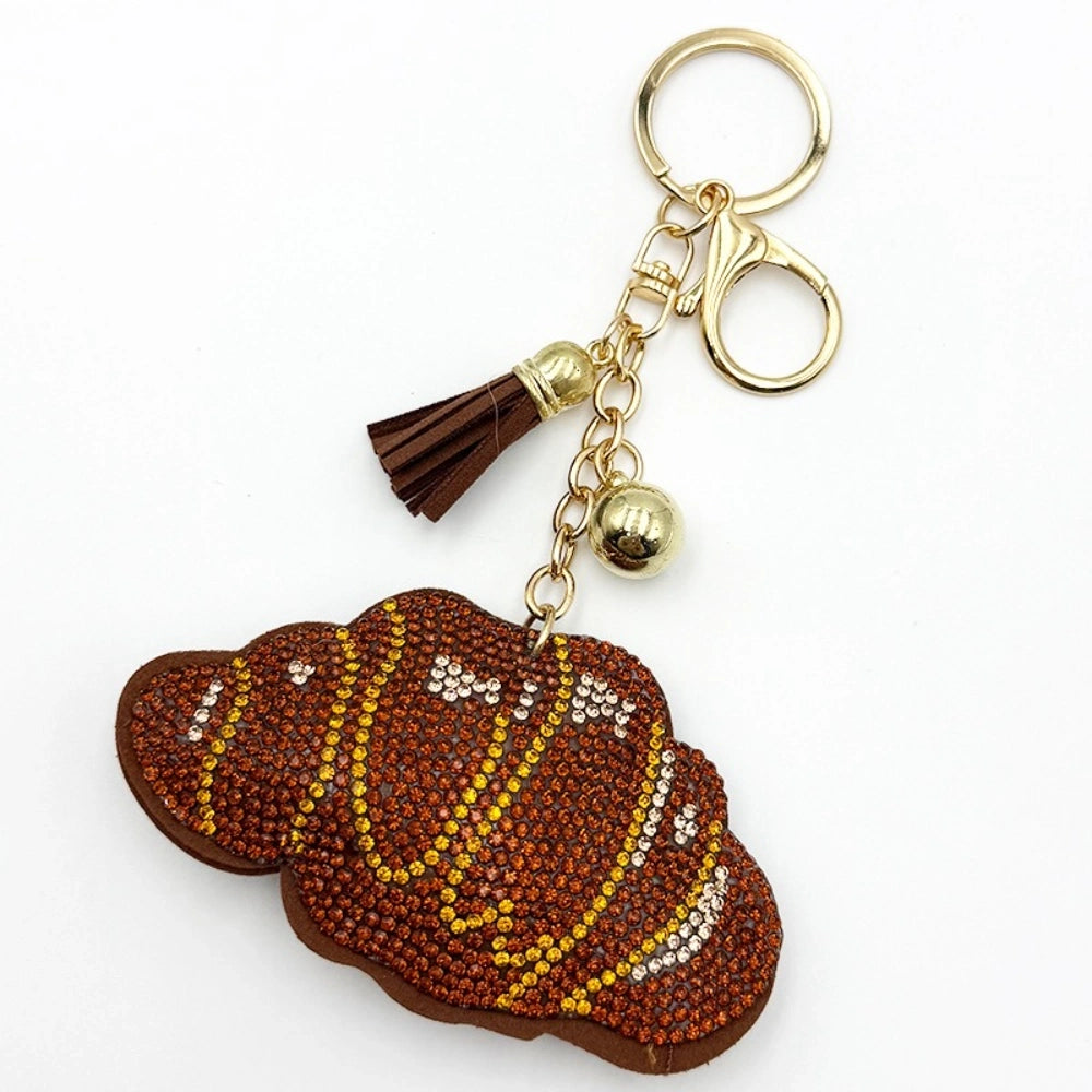 Crystal rhinestone concha pan dulce bread keychain charm with brown and yellow gemstones, gold lobster clasp, chain, tassel, and bell accent on white background.