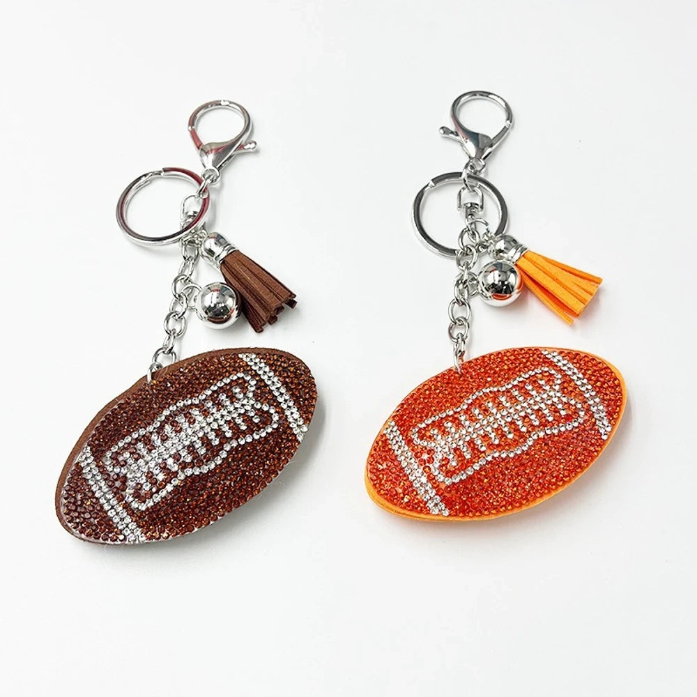 Two rhinestone-encrusted football shaped keychain charms with lobster clasp and tassel, one brown and one orange, on white background.