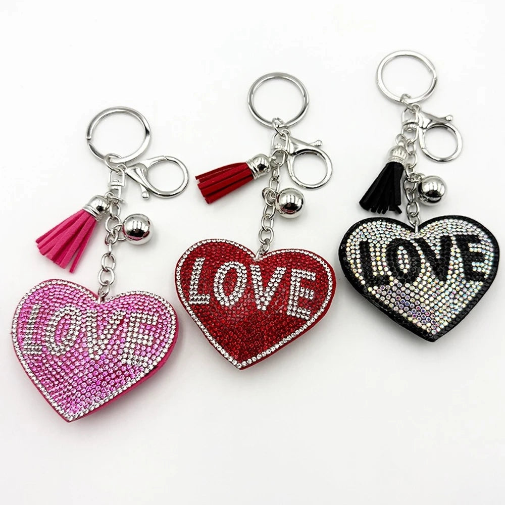 Three rhinestone-covered LOVE heart keychains in pink, red, and black with matching tassels and silver bell charms on white background.