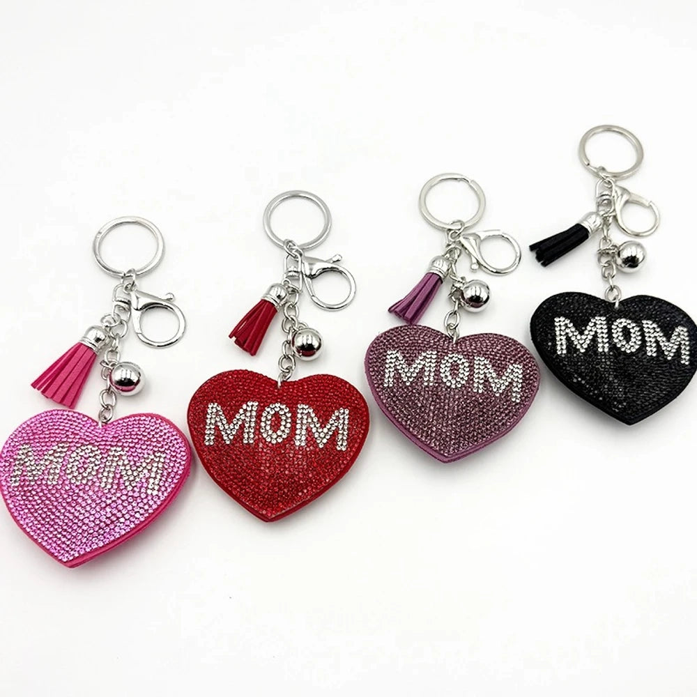 Four rhinestone MOM heart keychain charms in pink, red, purple, and black with tassel and silver ball accents on white background