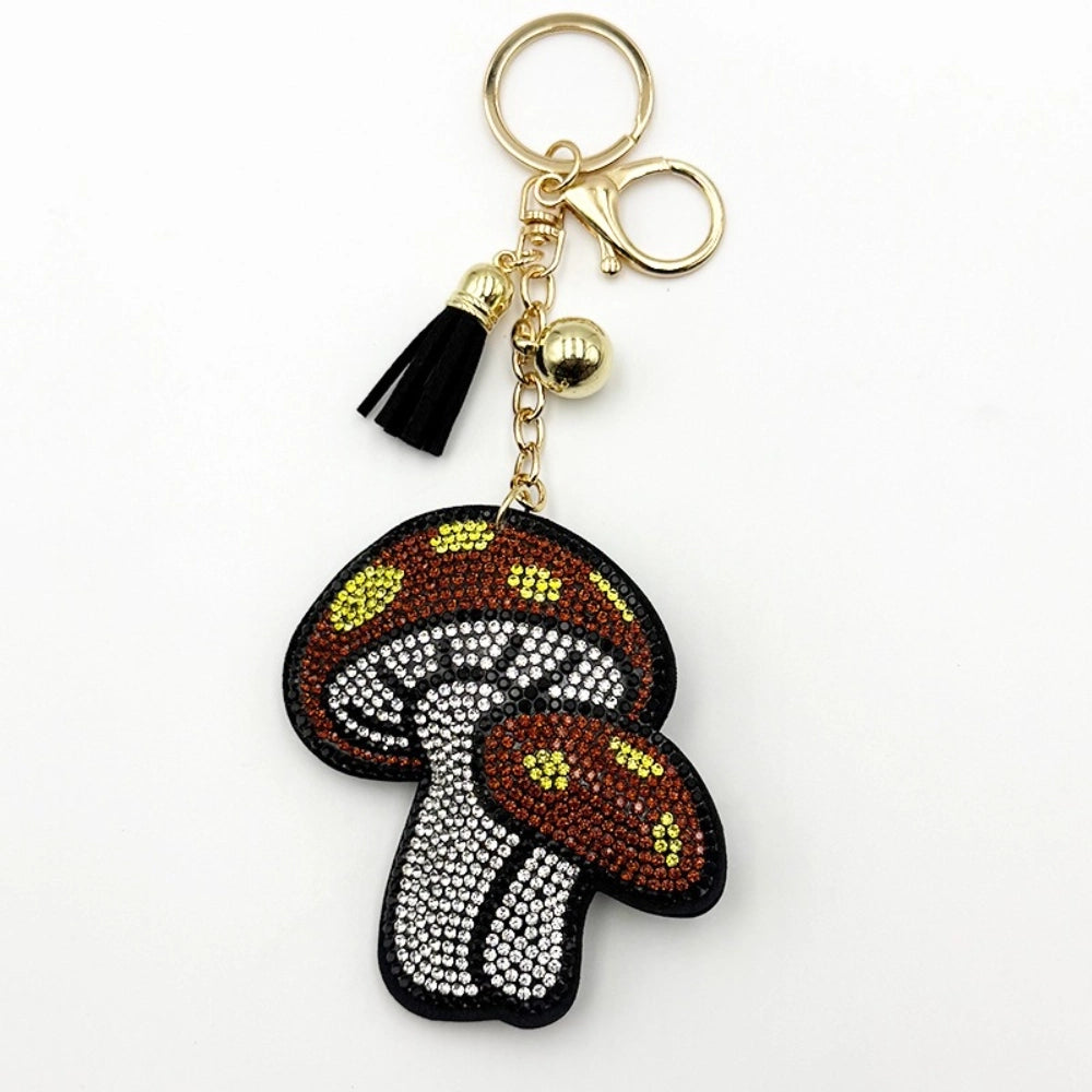 Rhinestone-encrusted mushroom keychain charm with brown, white, and yellow crystal beads, black tassel, and gold lobster clasp hardware on white background.