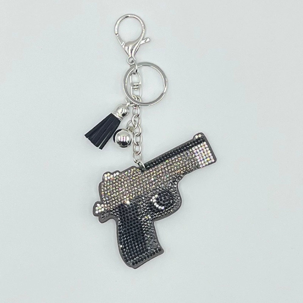 Rhinestone-encrusted pistol gun shaped keychain charm with silver lobster clasp, key ring, black tassel, and crystal AB and black rhinestone details on white background.