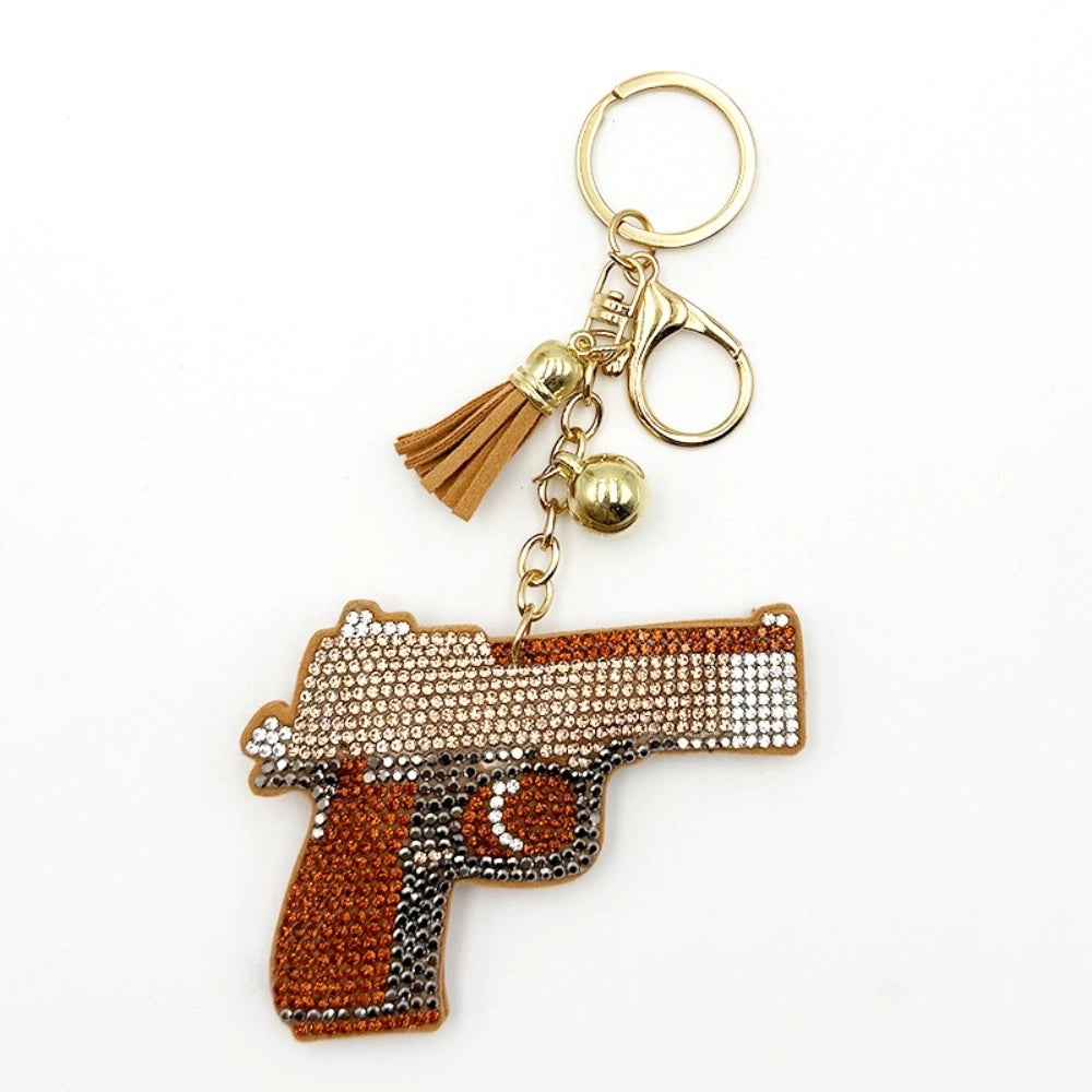 Brown and gold rhinestone-encrusted pistol gun keychain charm with tassel, bells, and gold lobster clasp on white background.