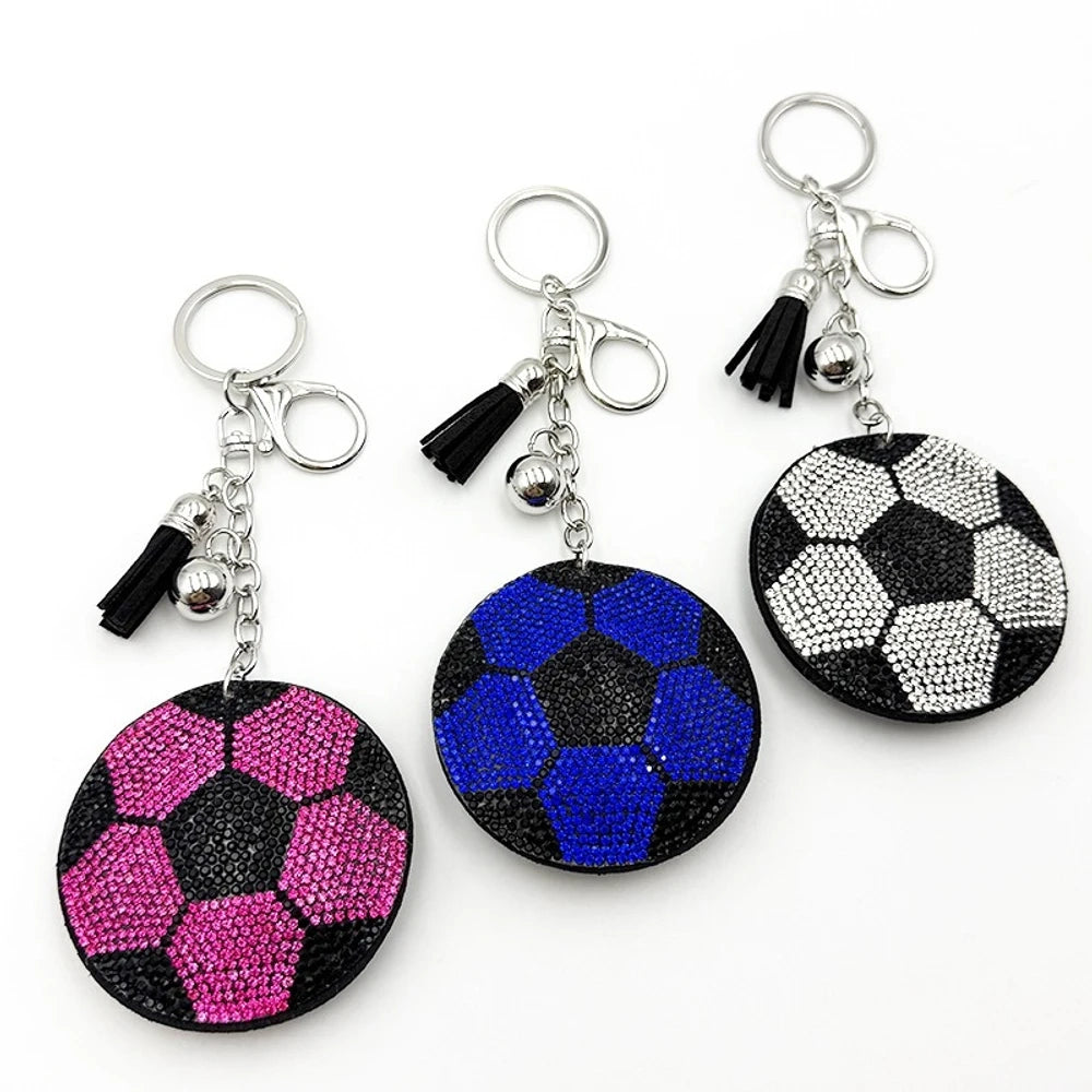 Three rhinestone soccer ball keychain charms in pink, blue, and silver/black with black tassels and silver lobster clasp hardware on white background.