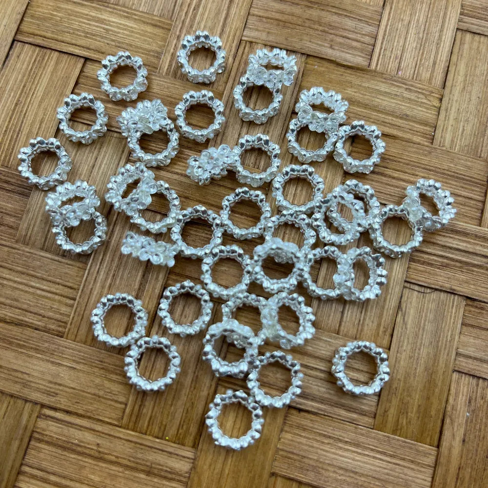 Multiple silver daisy flower ring metal spacers with textured scalloped edges arranged on a woven bamboo background, used for beadable pens, keychains, and DIY jewelry making.