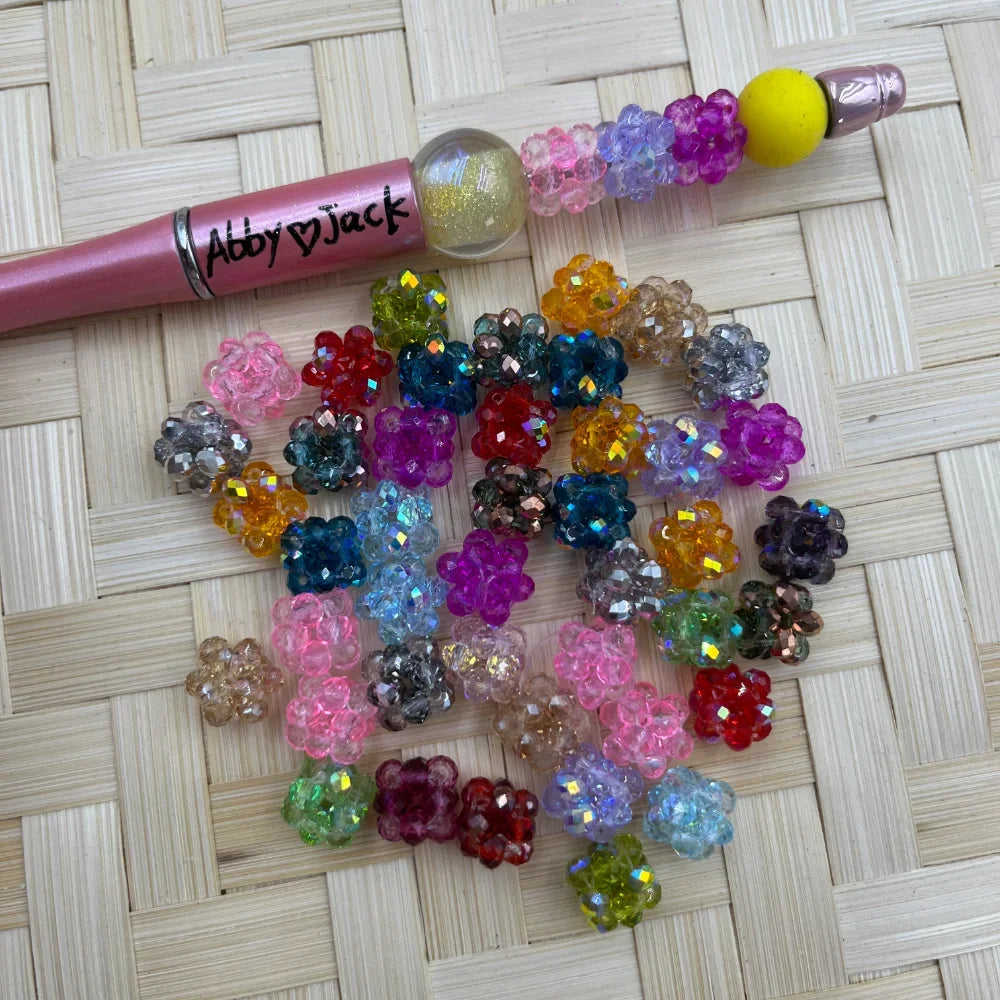 10MM assorted color crystal AB faceted cluster ball fancy beads scattered on wicker surface next to a pink beadable pen labeled Abby Jack
