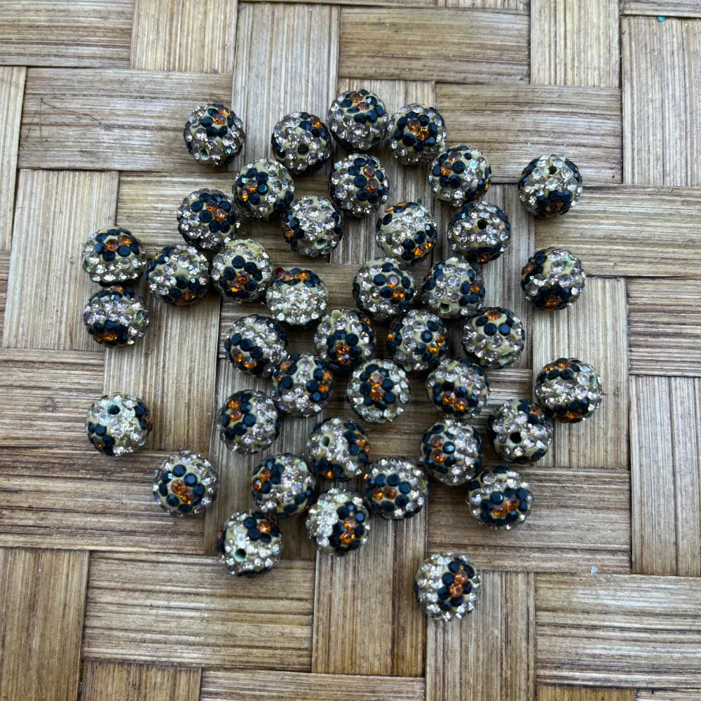 10MM leopard print clay rhinestone beads with black, amber orange, and clear crystal rhinestones arranged in a circle on a woven bamboo surface