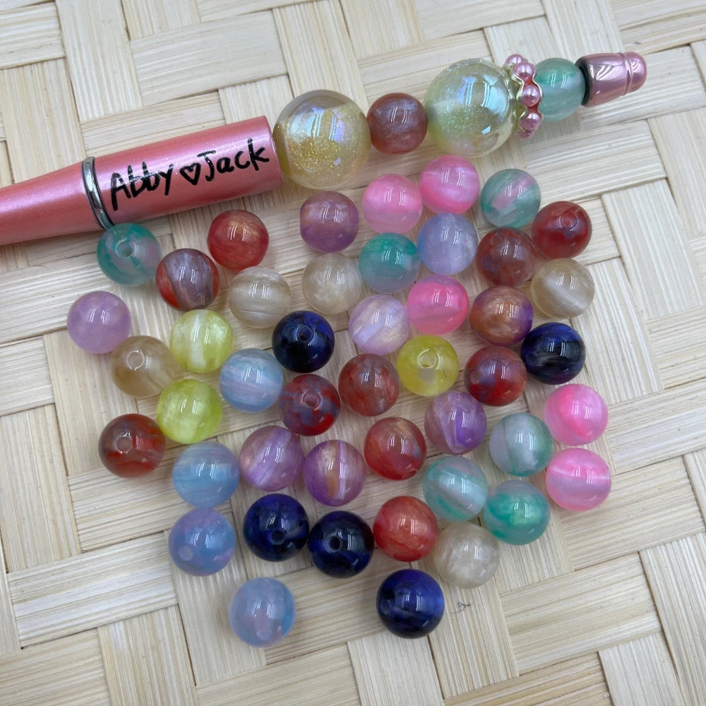 10MM multicolor marbled acrylic round beads in assorted pastel and bold swirl colors displayed next to a beadable pen on a woven surface.