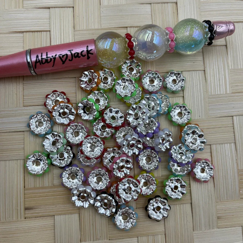 10MM silver daisy metal spacer beads with mixed color edge accents next to a decorated beadable pen