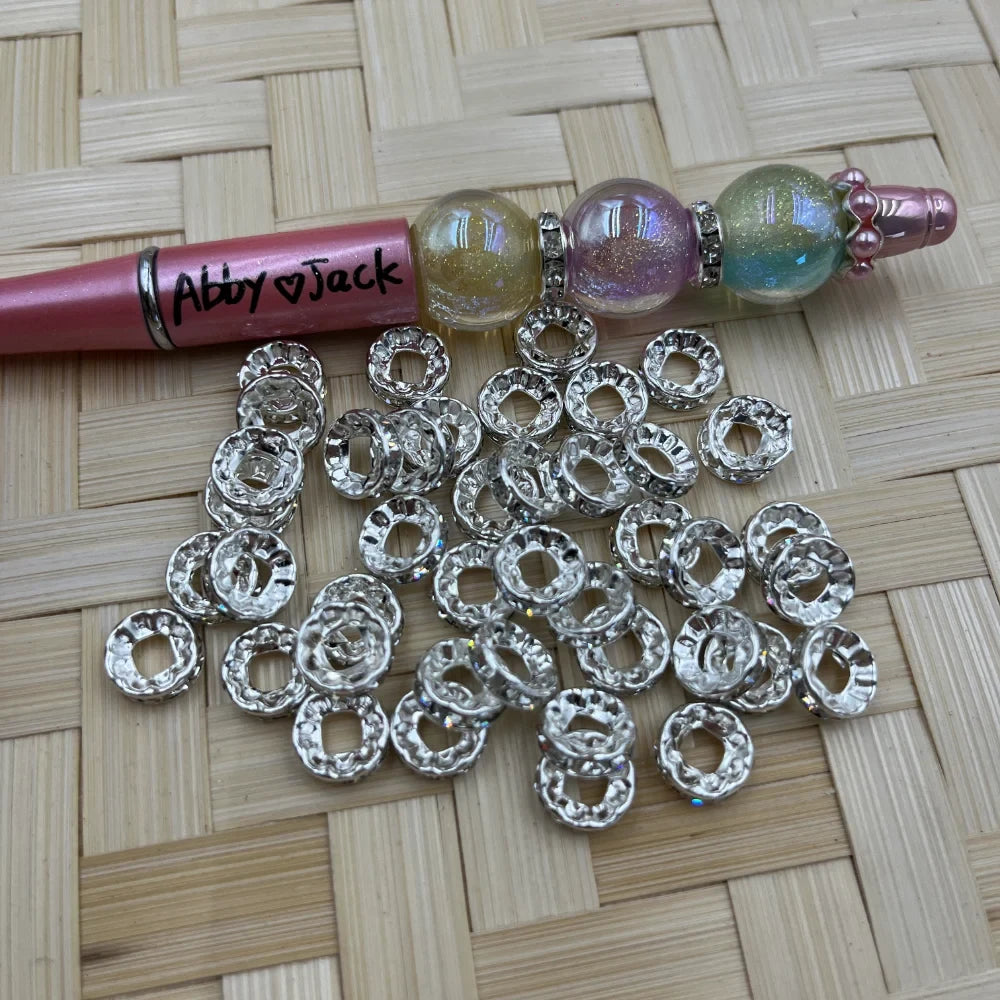 10MM silver rhinestone metal spacer beads beside a decorated beadable pen on a woven background