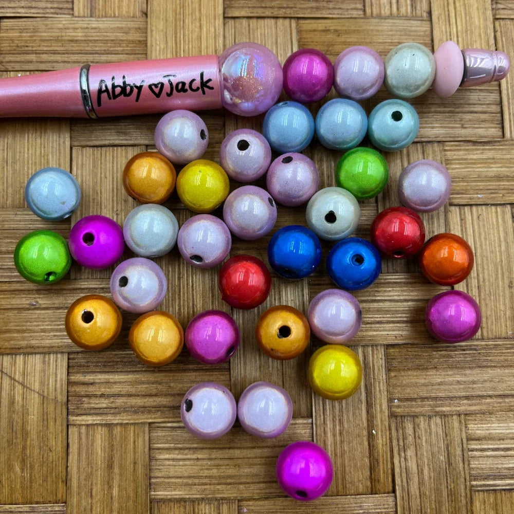 Assorted 12MM magic miracle acrylic beads in multiple colors including pink, blue, yellow, orange, green, red, and purple, displayed next to a beadable pen on a wicker surface.