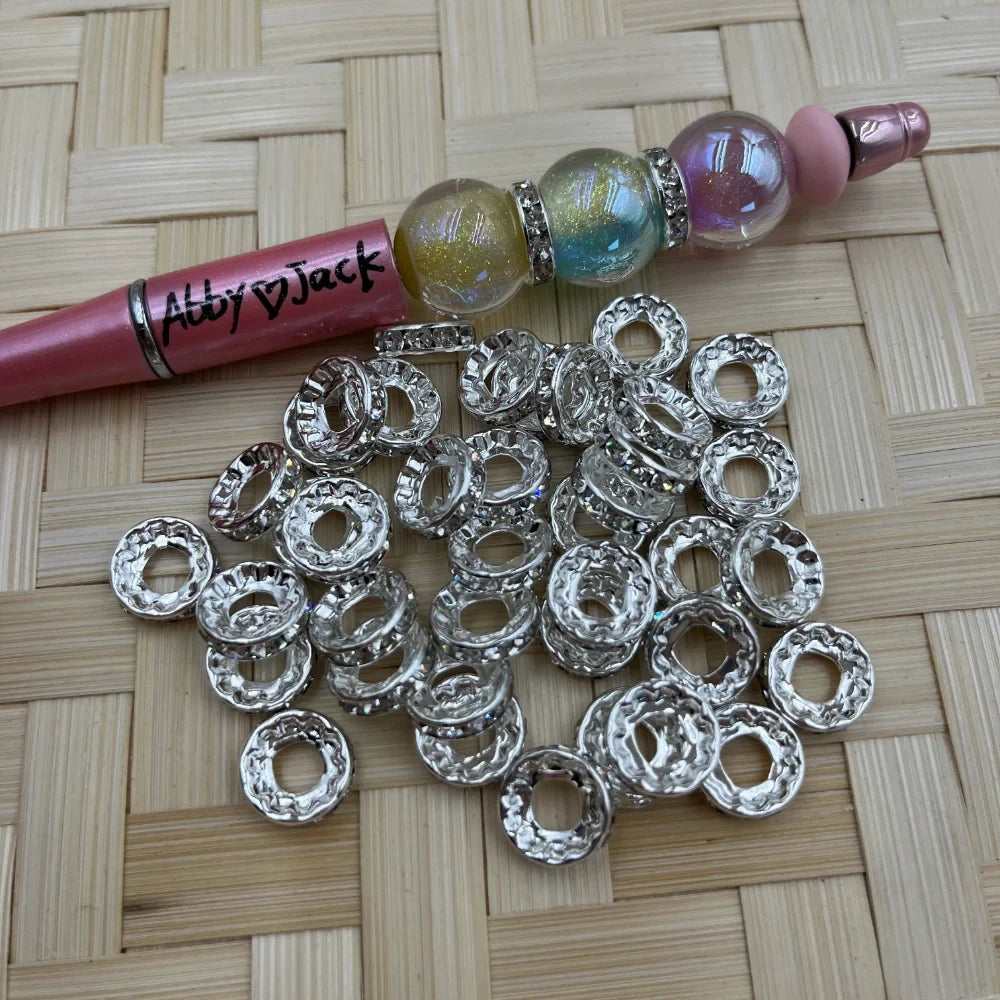 Pile of 12MM hammered donut silver tone metal spacer beads beside a decorated beadable pen