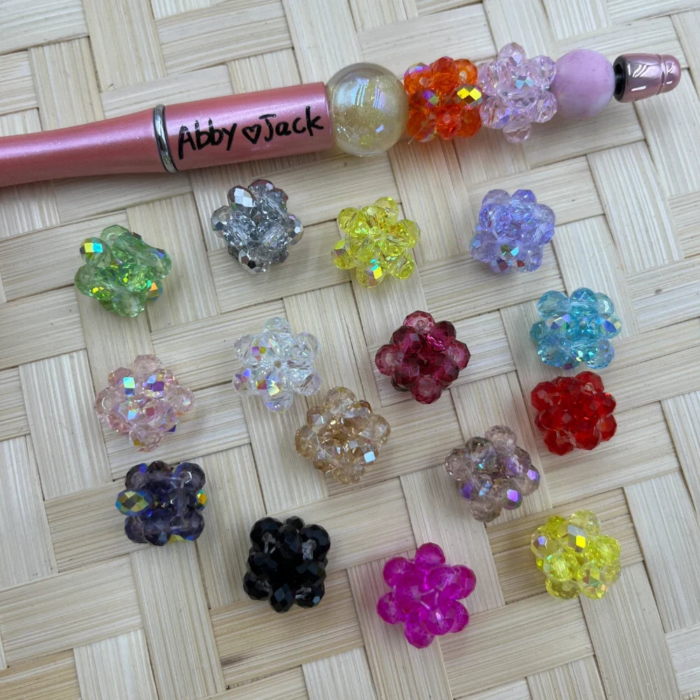 14MM crystal cluster ball fancy beads in assorted colors including pink, red, yellow, purple, teal, black, and clear AB finish, displayed on woven bamboo surface next to a beadable pen.