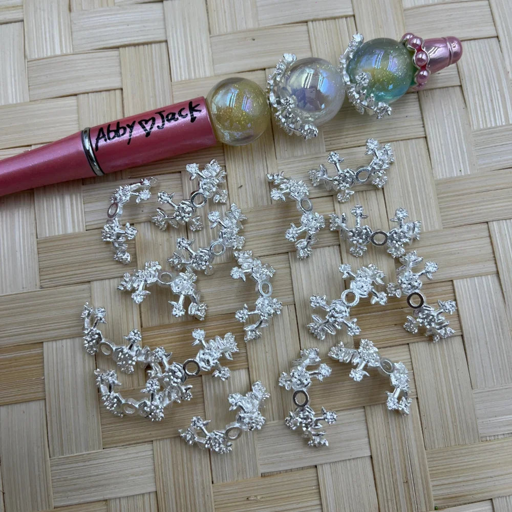 Silver 3D floral alloy bead caps beside a pink beadable pen with iridescent round beads on a woven mat